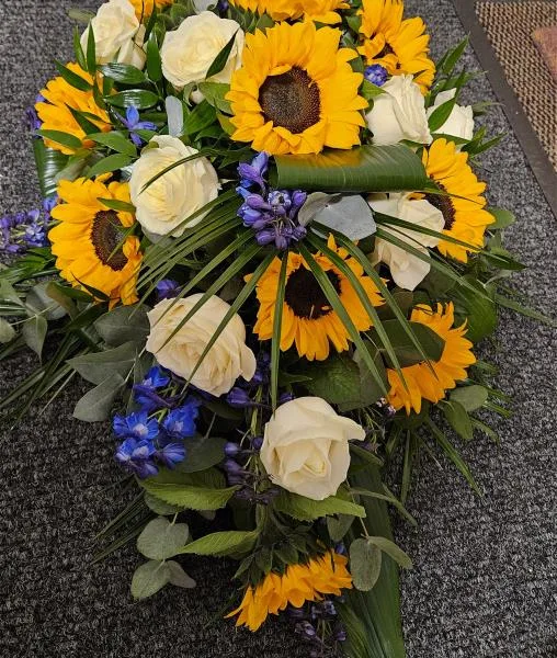 Tropical Grace Sunflower Teardrop Oasis Tribute — A soothing composition of vibrant sunflowers and lush tropical greenery, this teardrop casket spray