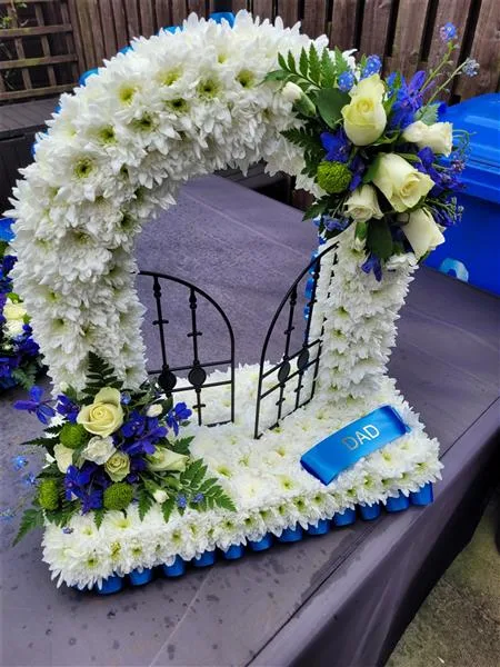 Gates of Heaven — A pair of black gates framed by a flower arch and base, shown in fresh white chrysanthemums with a b