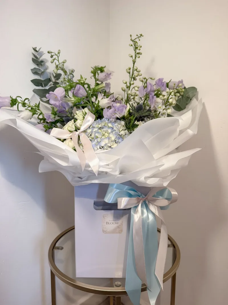 The Meadow Romance Bouquet — A dreamy arrangement of delicate lilac, soft blue and ivory blooms, thoughtfully combined with roman
