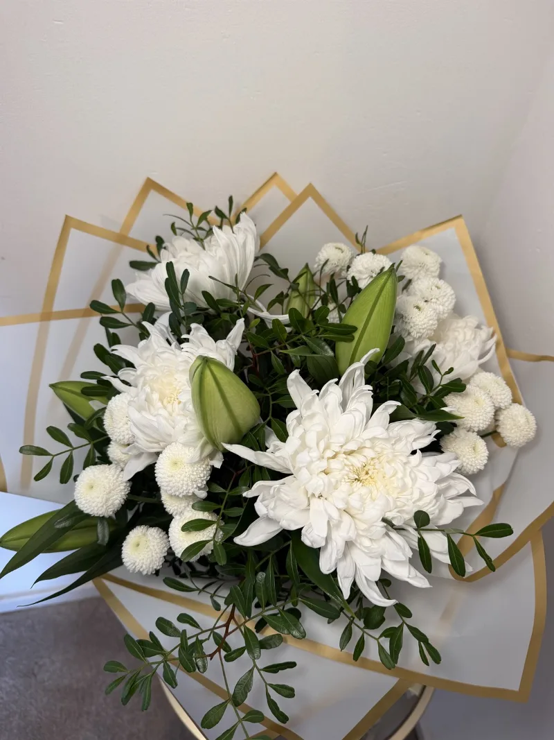 The Sympathy Bouquet — A timeless arrangement of white lilies, chrysanthemums and delicate white santini blooms, complement