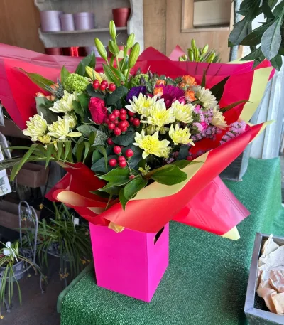 The Carnival — Red, yellow and white blooms with hypericum berries, arranged in a bright pink gift box.