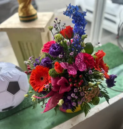 The Bright Hat Box — A bright arrangement of roses, gerbera, delphinium and lisianthus in a hat box, finished with a bow.