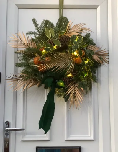 The Golden Palm — Fresh foliage with gold palm leaves, dried oranges and fairy lights, finished with a green ribbon.
