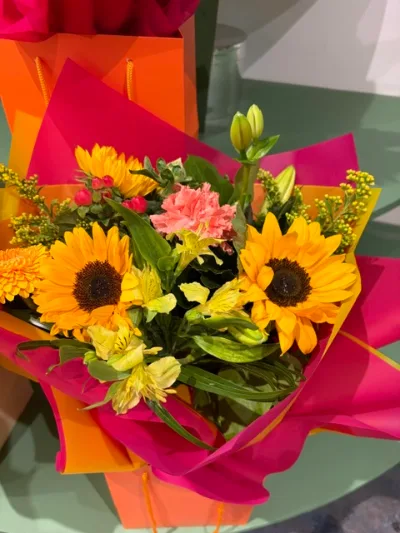 The Sunflower — Sunflowers, alstroemeria and a pink carnation with fresh greenery, wrapped in pink and orange.