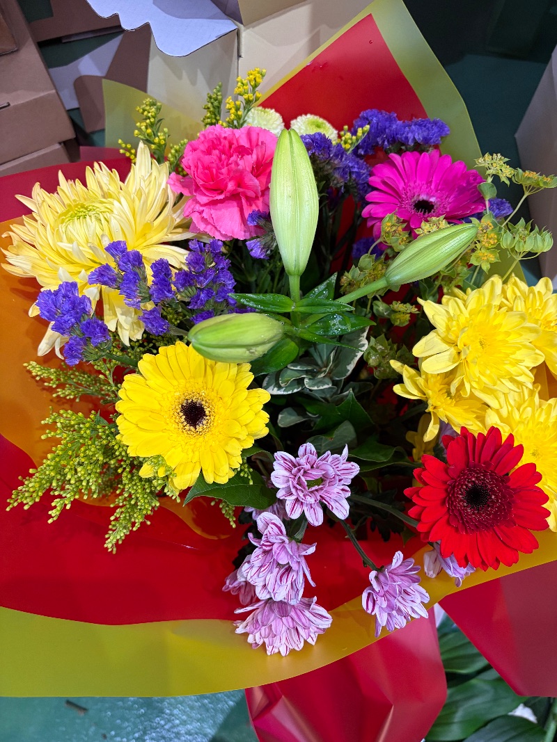 Tutti Frutti — A colourful mixture including a lily, chrysanthemum and gerberas hand tied in water in a bag. Due to