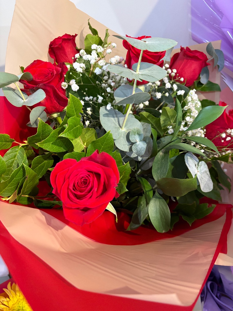 Romantic — 6 red roses with seasonal foliage wrapped in cellophane in water in a box.